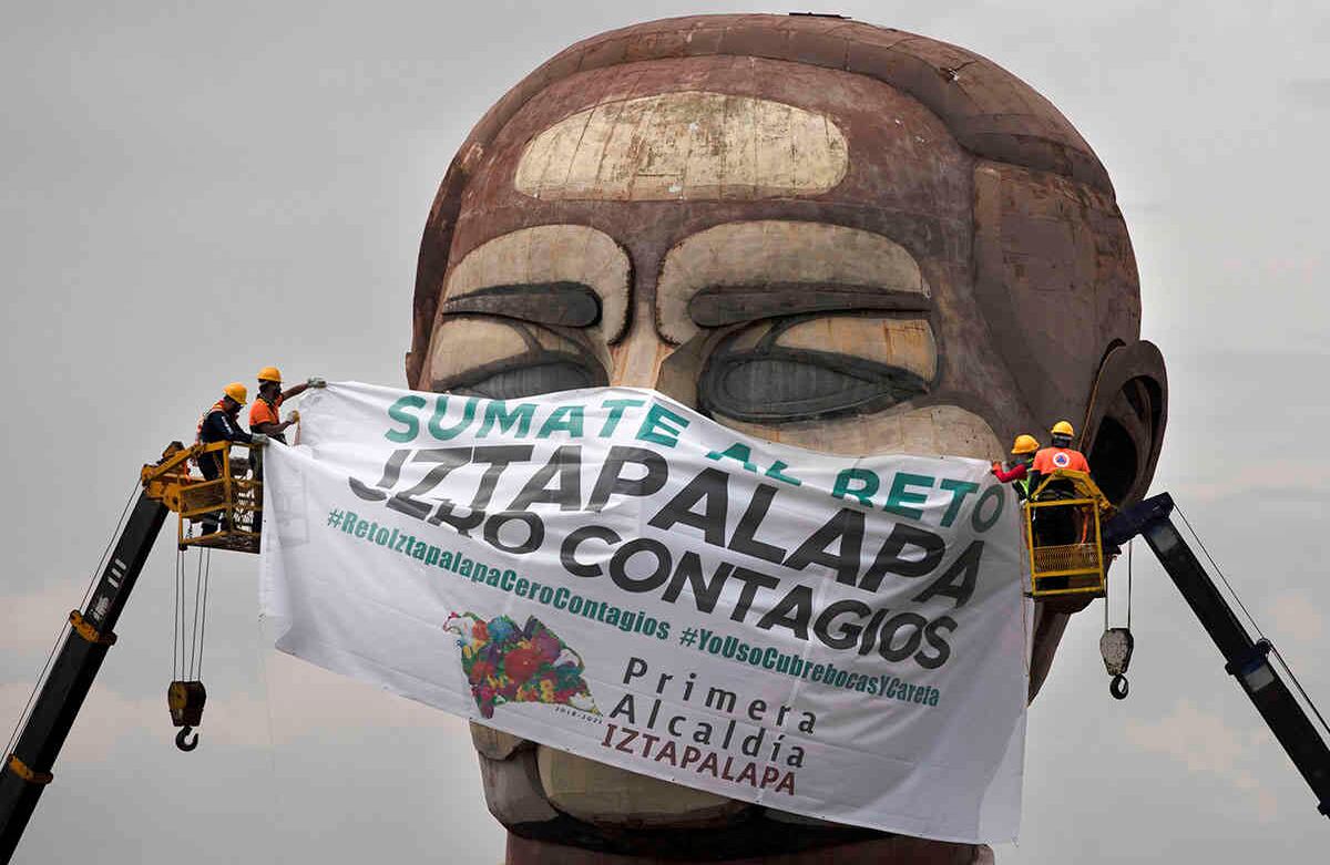 Los trabajadores de la ciudad colocan una mascarilla gigante en el Museo Cabeza de Juárez con un texto escrito en español que dice: “Únete al desafío de Iztapalapa. Cero infecciones”. Imagen tomada en Ciudad de México el miércoles 12 de agosto de 2020. El museo construido en 1976 es un enorme monumento multicolor que representa al vigésimo sexto presidente de México, Benito Juárez. Foto: Marco Ugarte / AP  