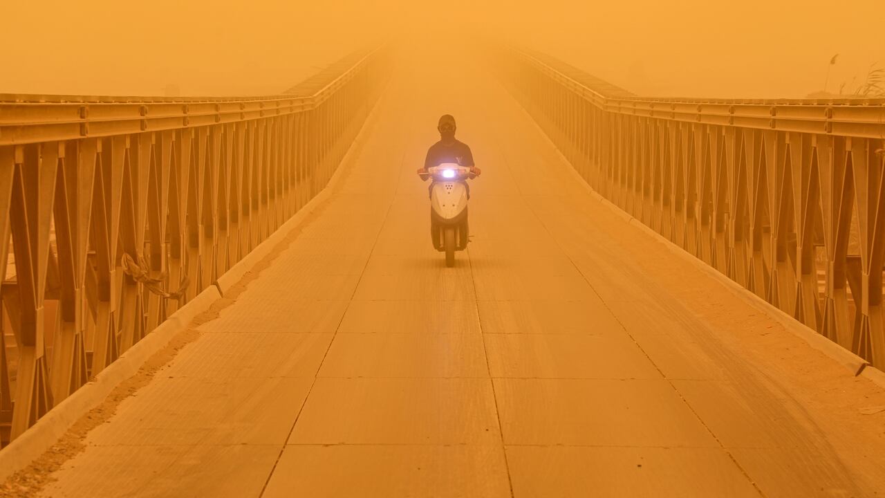 Un automovilista conduce un scooter a lo largo de un puente en la ciudad de Nasiriyah, en la provincia de Dhi Qar, en el sur de Irak, el 16 de mayo de 2022 en medio de una fuerte tormenta de polvo. (Foto de Asaad NIAZI / AFP)