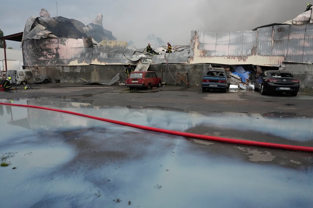 Bomberos extinguen un incendio junto a leche derramada en primer plano, después de que misiles rusos impactaran en un almacén de alimentos cerca de Kiev, Ucrania, el miércoles 5 de agosto de 2026. (Foto AP/Efrem Lukatsky)