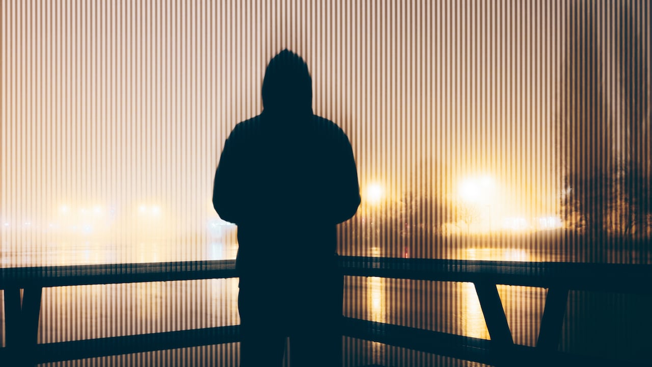 Hooded figure, back to camera. Looking out on a city at night. On a mysterious foggy night. With a blurred abstract edit