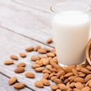 Nueces de almendras en tazón de madera y leche de almendras en vidrio sobre fondo de mesa de madera.