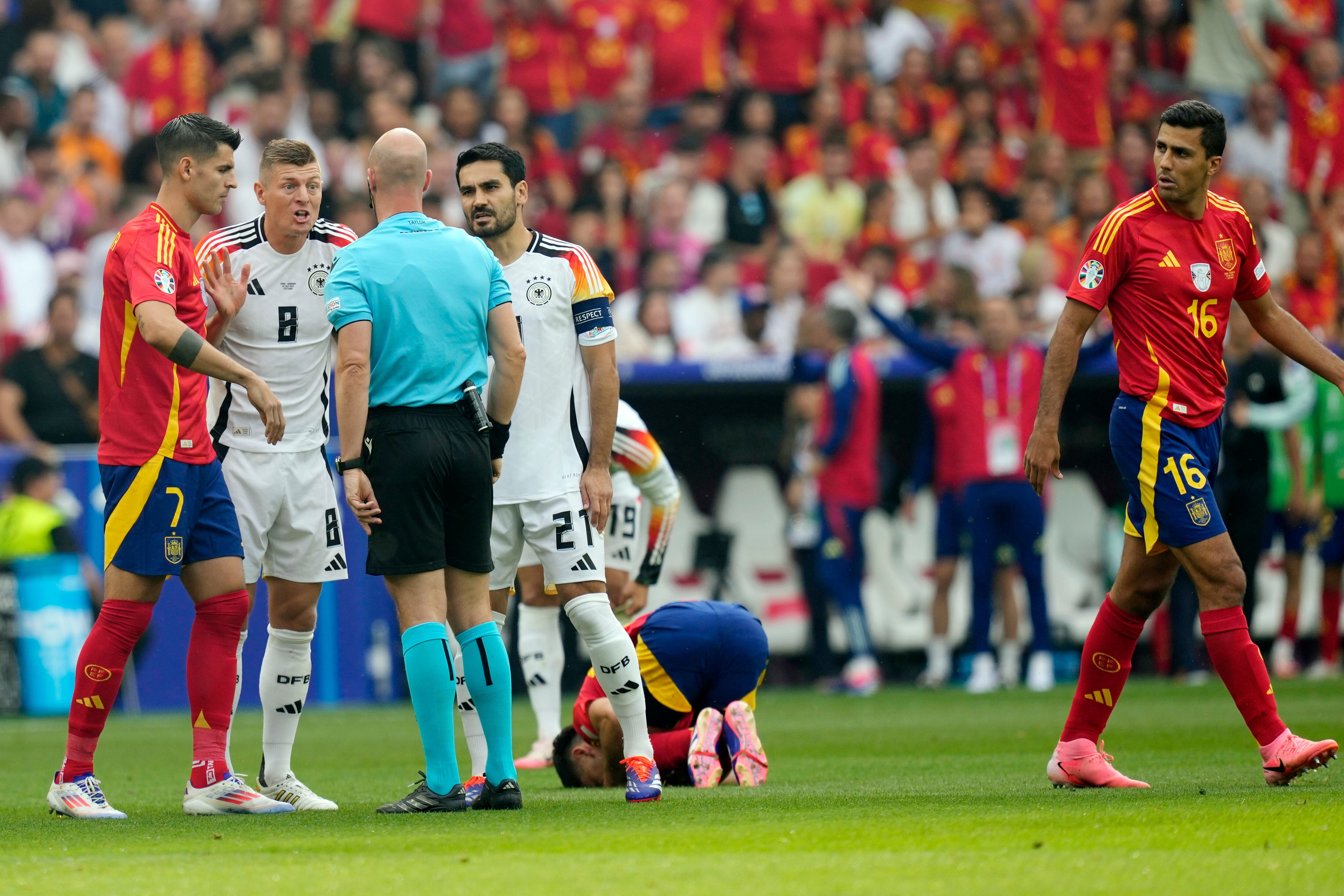 Germany's Toni Kroos (8) and Ilkay Gundogan (21) speak with referee Anthony Taylor, of England, during a quarterfinal match between Germany and Spain at the Euro 2024 soccer tournament in Stuttgart, Germany, Friday, July 5, 2024. (AP Photo/Antonio Calanni)