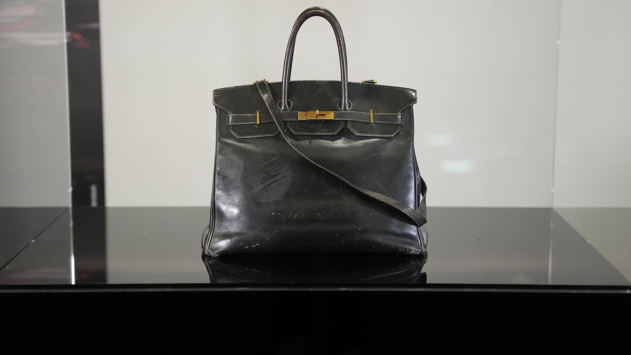 Primer plano del bolso Hermès Birkin original de piel negra de Jane Birkin, que muestra desgaste visible, una estructura suavizada, esquinas desgastadas y herrajes dorados oxidados, incluyendo una larga correa de hombro que rodea las asas.