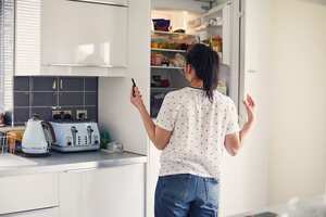 Woman looking in the fridge whilst using smartphone to do her food shopping online
