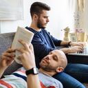 Pareja gay leyendo un libro en un sofá.