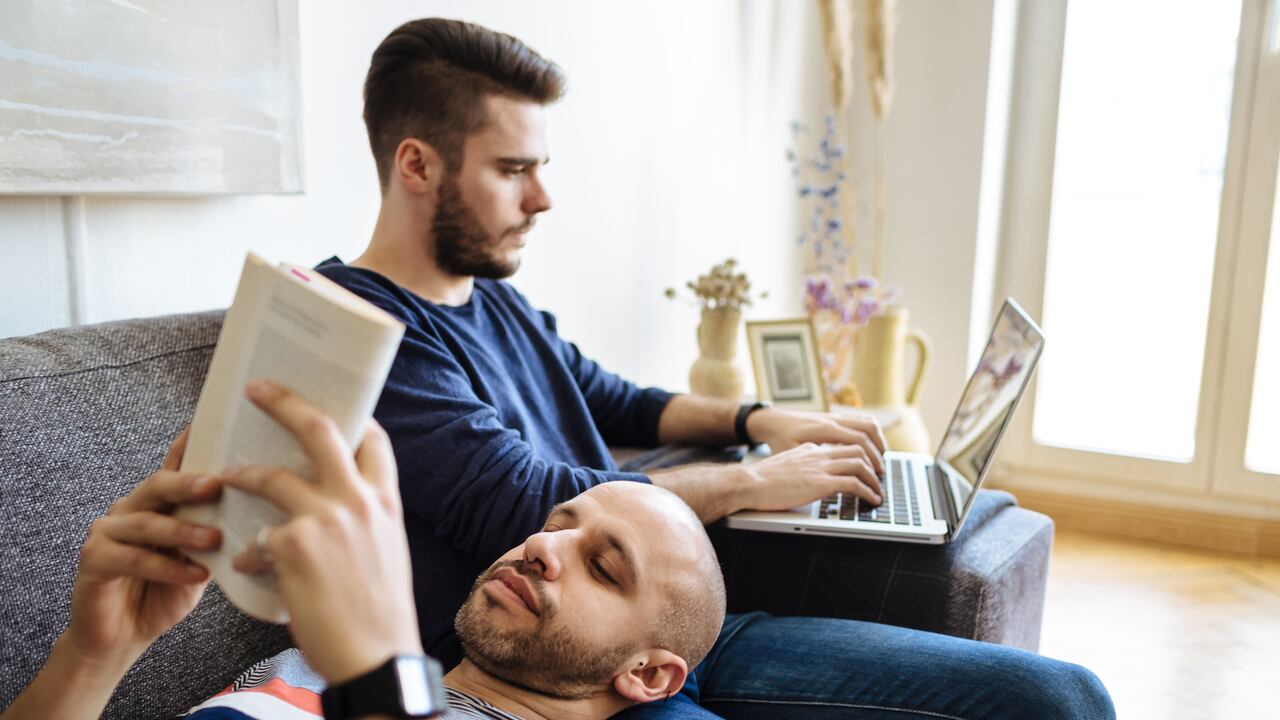 Pareja gay leyendo un libro en un sofá.