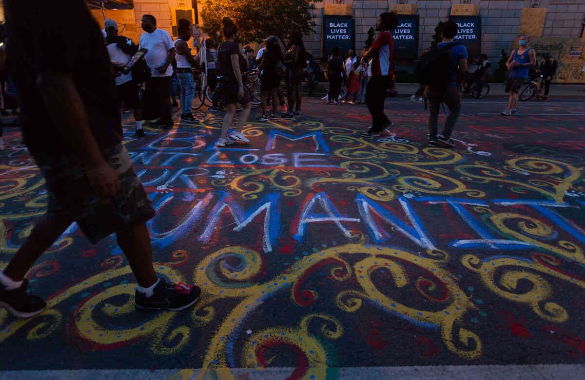 Un grupo de gente se congrega festivamente la noche del 9 de junio sobre H St NW enfrente de la reja que rodea Lafayette Square. Además de cubrir la reja de letreros durante los días pasados, el pavimento sobre ese tramo de 16th St NW ha sido cubierto de mensajes. Imagen tomada el 09 de junio de 2020, Washington DC- Foto María Luz Bravo