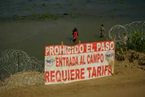 Migrants walk past the site where workers are assembling large buoys to be used as a border barrier along the banks of the Rio Grande in Eagle Pass , Texas, Tuesday, July 11, 2023. The floating barrier is being deployed in an effort to block migrants from entering Texas from Mexico. (AP Photo/Eric Gay)