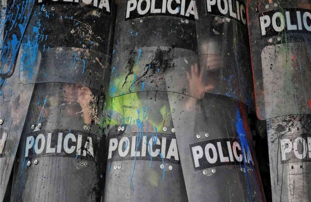 Policías se protegen de las bombas de pintura y piedras que les arrojan los encapuchados.