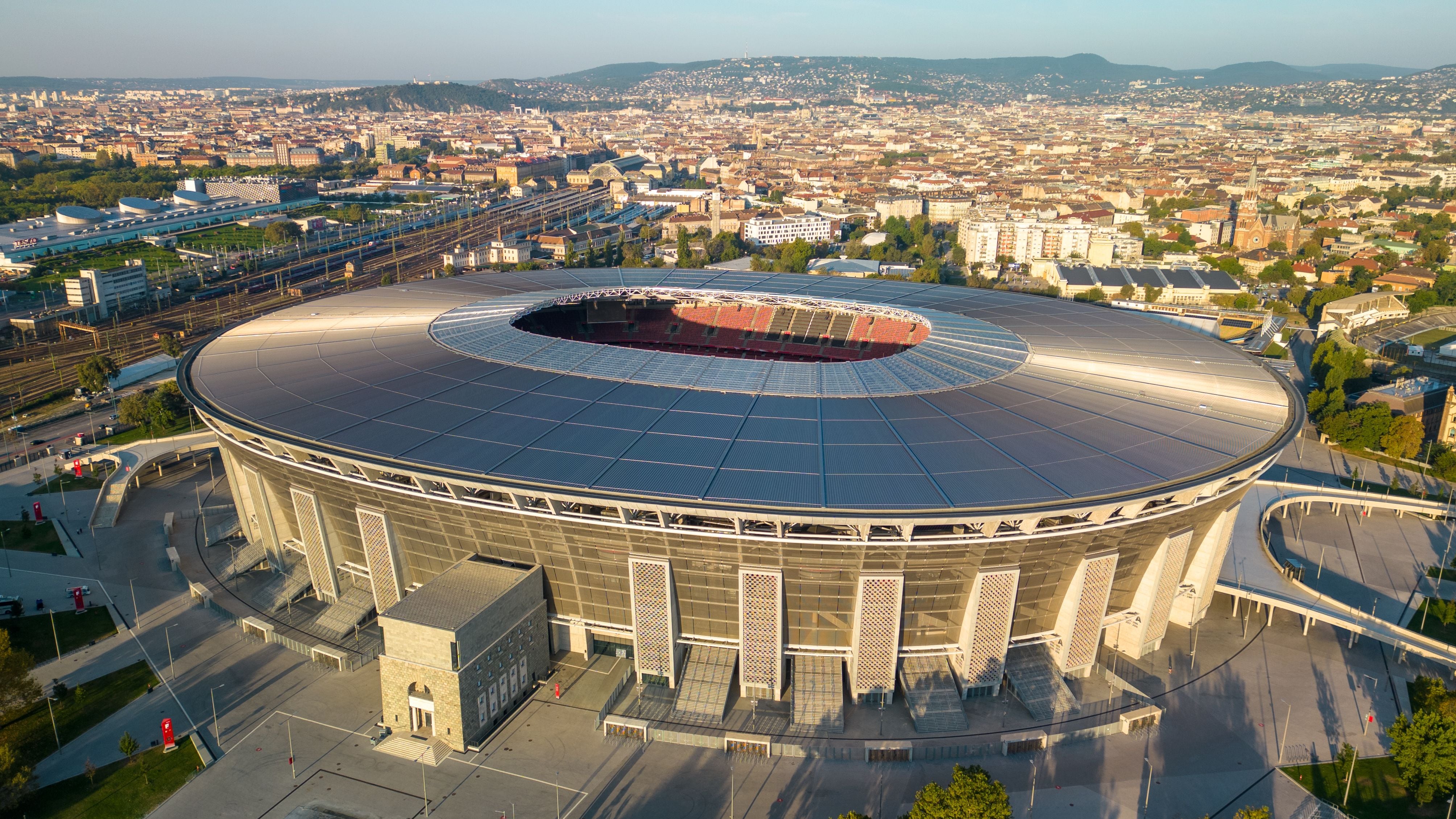Perspectiva aérea del estadio Puskas Arena en Budapest con el horizonte del centro y líneas de tren al fondo