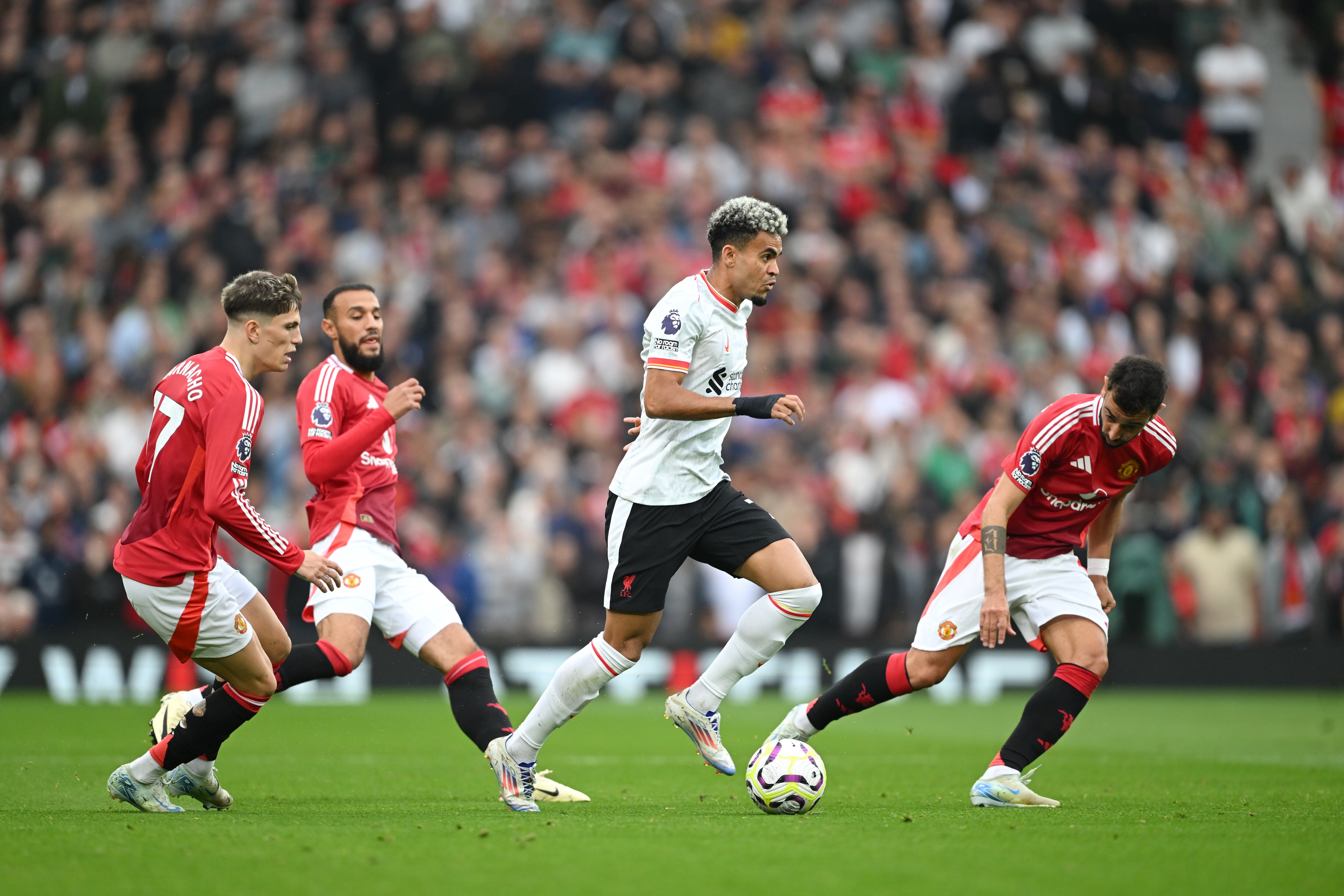 MANCHESTER, ENGLAND - SEPTEMBER 01: Luis Diaz of Liverpool runs with the ball under pressure from Alejandro Garnacho and Bruno Fernandes of Manchester United during the Premier League match between Manchester United FC and Liverpool FC at Old Trafford on September 01, 2024 in Manchester, England. (Photo by Michael Regan/Getty Images)