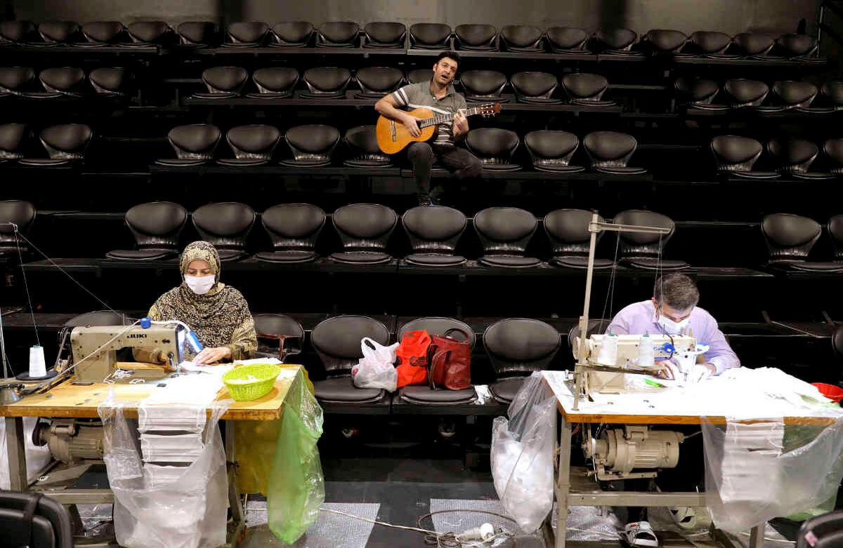 Voluntarios cosen máscaras faciales, mientras un guitarrista toca para los voluntarios, en la sala de teatro Hafez, en el centro de Teherán, Irán, el 15 de abril. Irán tiene 79.494 casos de contagio registrados. Foto: Ebrahim Noroozi/ AP