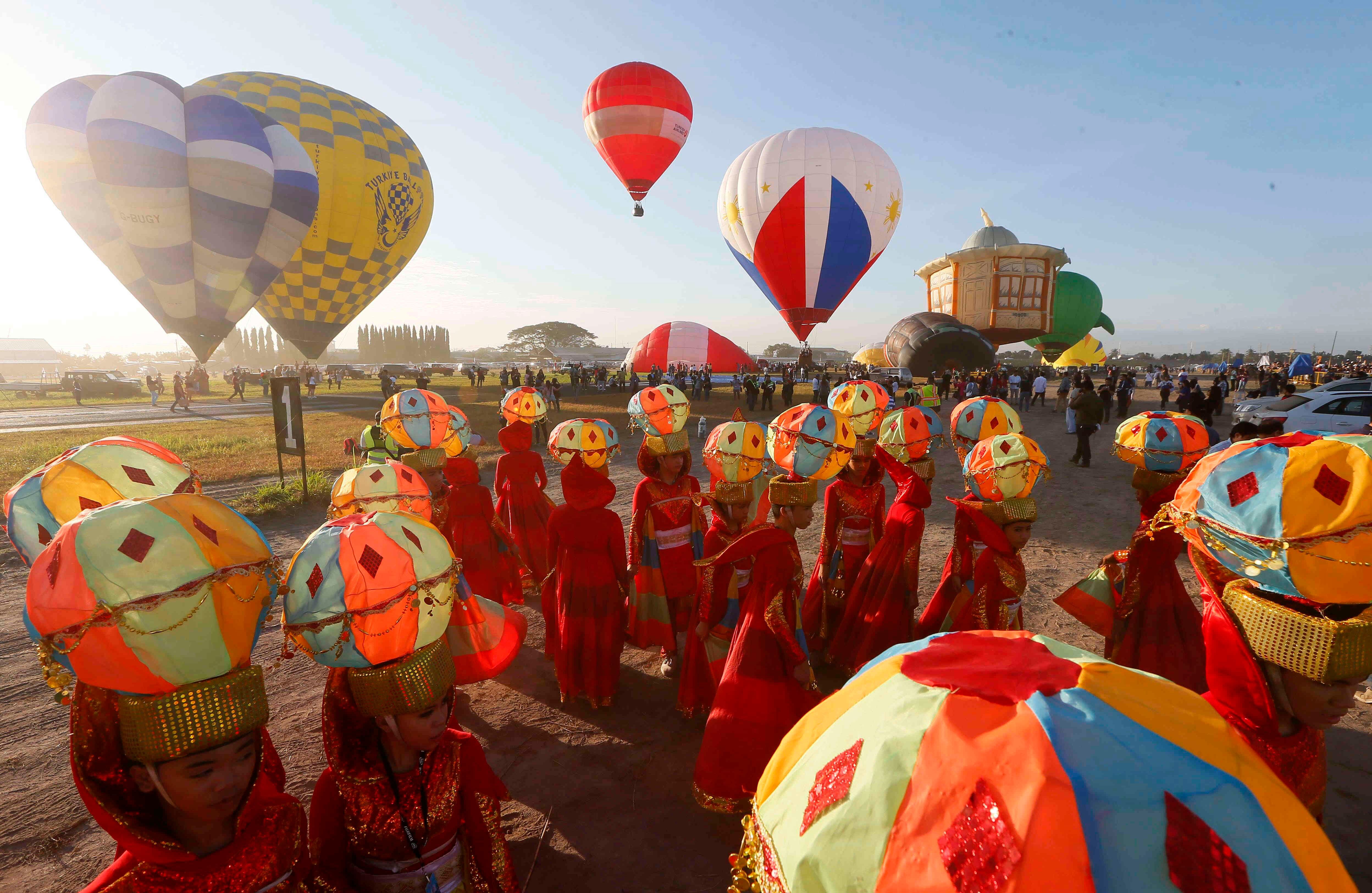 Los actores que llevan trajes de globo aerostático se preparan para su número cuando los aeróstatos despegan para perseguir al líder en el inicio del festival de Hot Air de 21 días en Clark, provincia de Pampanga, al norte de Manila, 9 de febrero de 2017. Veintinueve globos de aire caliente de diferentes países están participando en el festival. (AP Photo / Bullit Márquez)