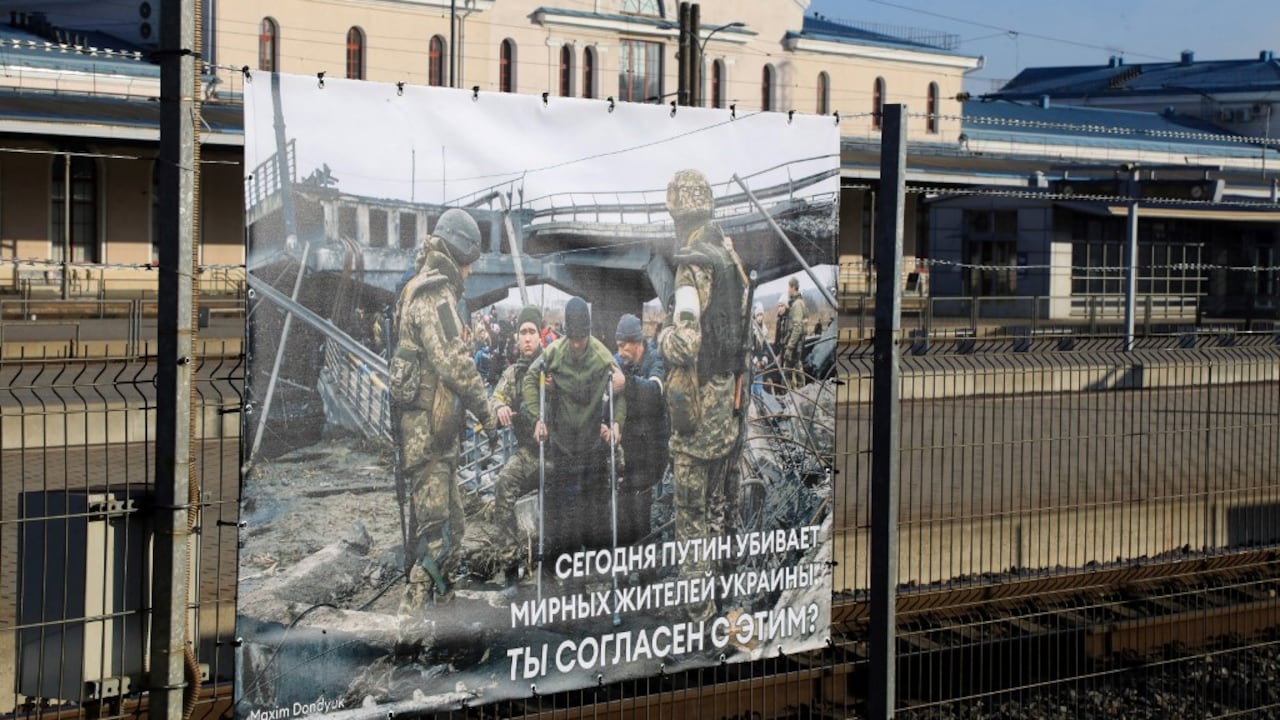 Una foto tomada por el fotógrafo ucraniano Maxim Dondiuk se ve junto a otras fotografías de la guerra de Rusia en Ucrania como parte de una exhibición en la estación de tren en Vilnius, Lituania, donde transitan los trenes desde Moscú a Kaliningrado, el 25 de marzo de 2022 (Foto de PETRAS MALUKAS / AFP)