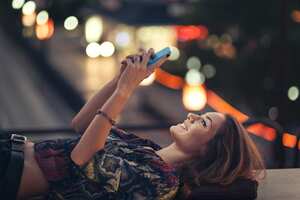 Smily girl chatting with friends, while laying on a bridge, above evening traffic. Beautiful bokeh - fast lens used.