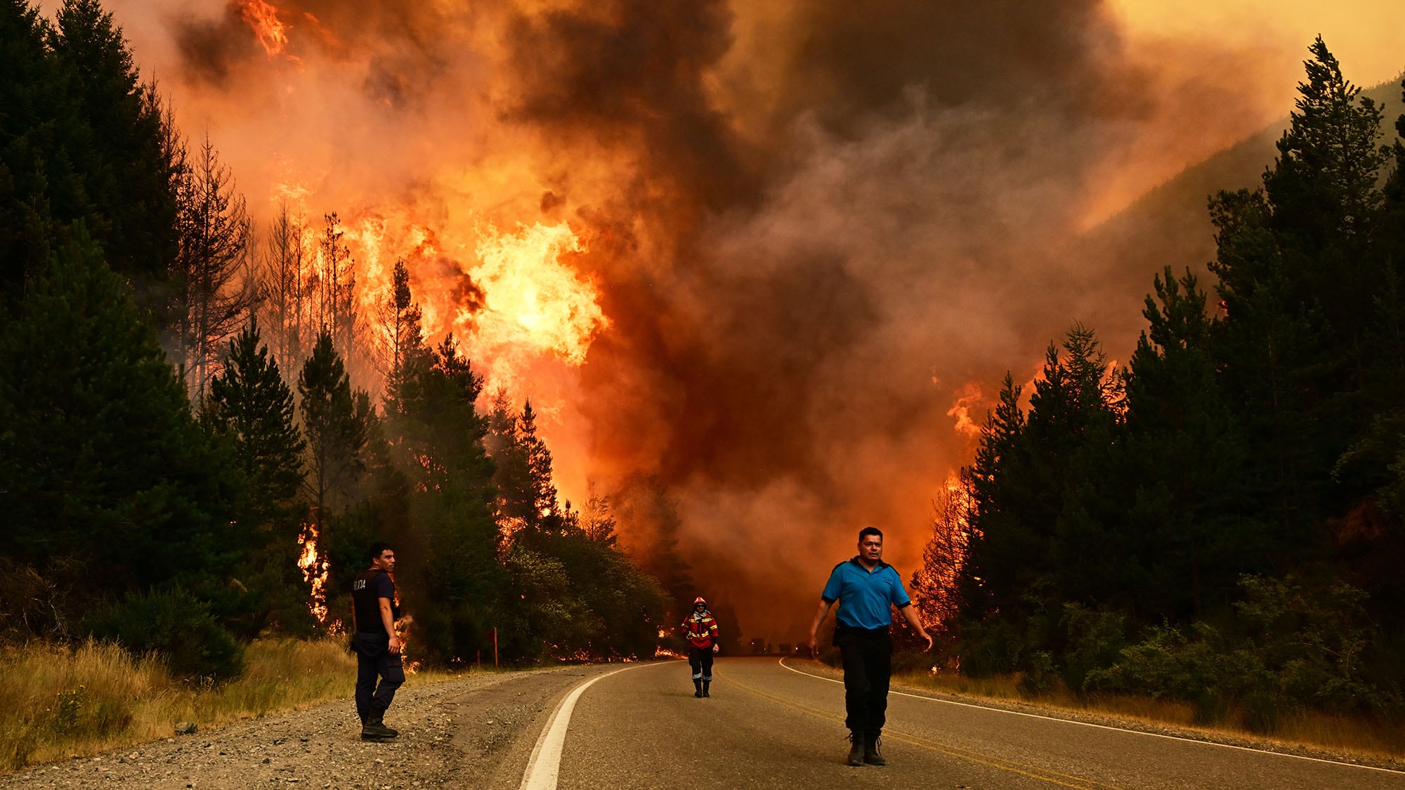 Bomberos caminan por una carretera durante un incendio forestal en El Hoyo, Patagonia, Argentina. Jueves 8 de enero de 2026.