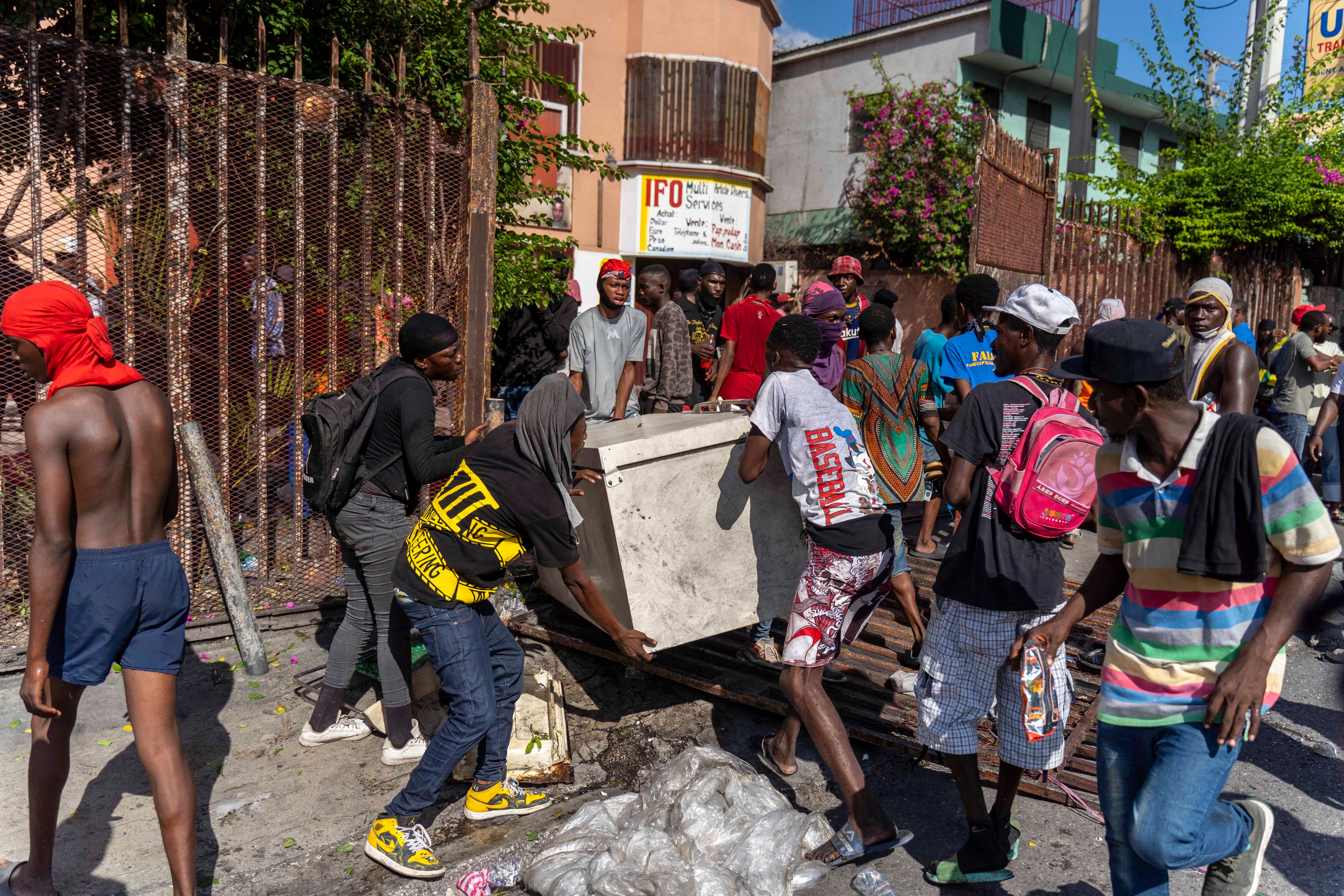 Los hombres huyen con bienes saqueados durante una protesta contra el primer ministro haitiano Ariel Henry pidiendo su renuncia, en Port-au-Prince, Haití, 10 de octubre de 2022. - Las protestas y los saqueos han sacudido el ya inestable país desde el 11 de septiembre, cuando el primer ministro Ariel Henry anunció un aumento en el precio del combustible. (Foto de Richard Pierrin / AFP)