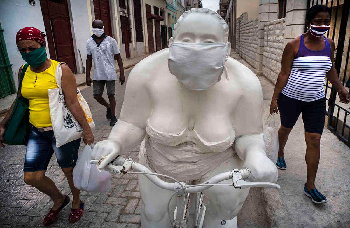 Peatones caminan por una de las esculturas de Xu Hongfei (Fat Ladies), que un anónimo adornó con una máscara para promover el distanciamiento social, en La Habana, Cuba, el 13 de mayo. Las autoridades cubanas exigen el uso de tapabocas a todas las personas que salen a la calle. Foto: Ramon Espinosa/ AP.