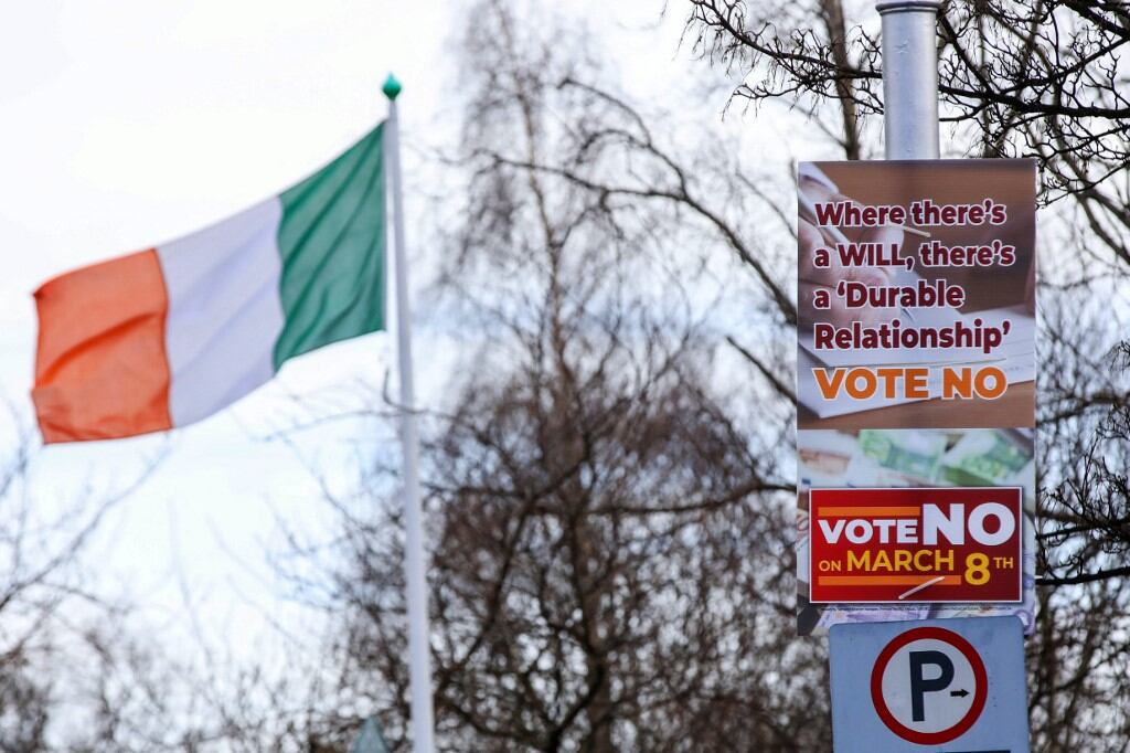 Se ven carteles de "No" en la calle frente a los edificios gubernamentales en Dublín, Irlanda, el 5 de marzo de 2024, antes del referéndum irlandés del viernes. Al fondo, la bandera del país. Irlanda se prepara para votar el viernes sobre las referencias constitucionales a la familia y el papel de la mujer en el hogar (Foto de PAUL FE / AFP)