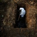 Un hombre con un traje de protección cava la tierra para enterrar el cuerpo de una persona que murió a causa de covid-19 en Gauhati, India