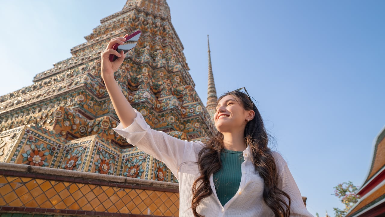 Joven turista en Bangkok tomándose una foto en un templo budista en Tailandia.
