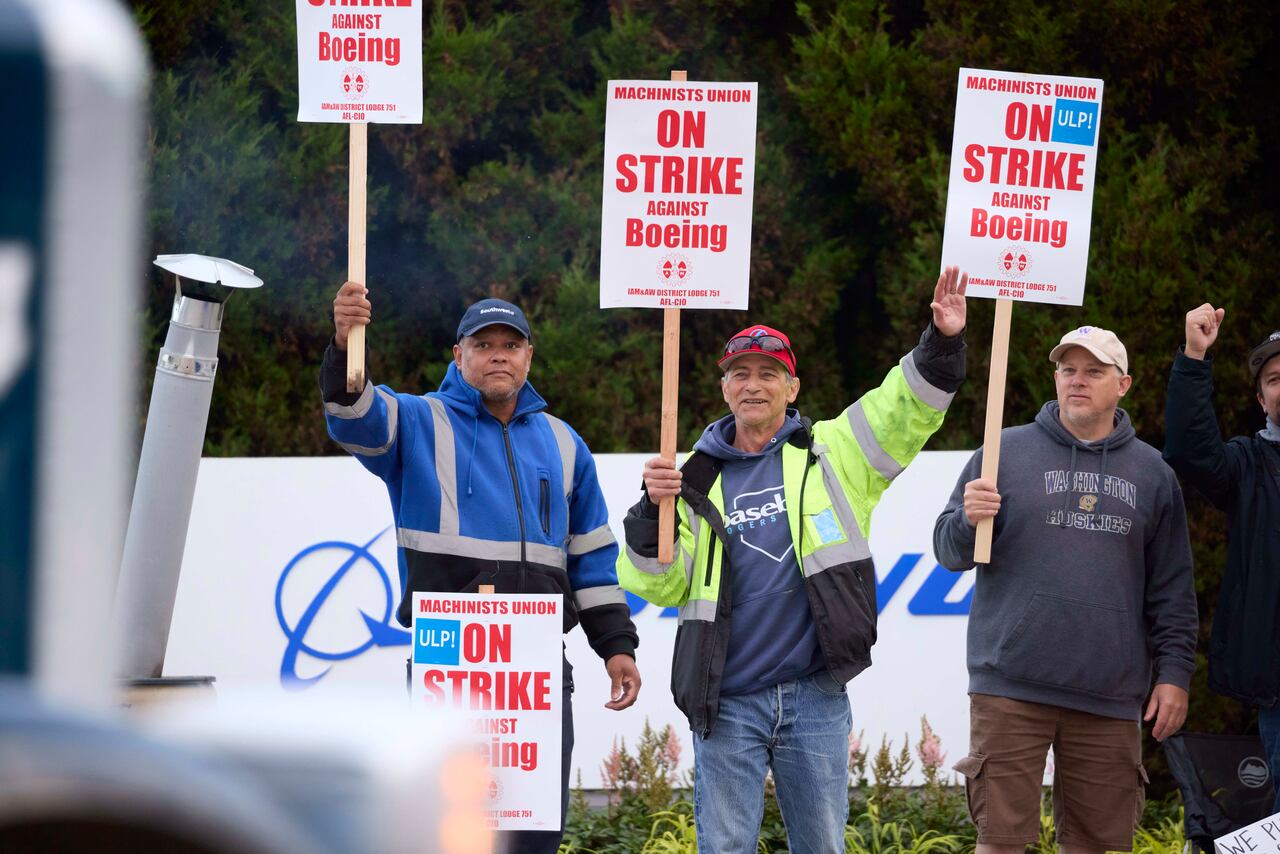Los miembros del Sindicato de Maquinistas de Boeing Steven Wilson, izquierda, Dave Hendrickson, centro, y Mark Erickson, derecha, saludan al tráfico que pasa mientras están en el piquete en la planta de ensamblaje de Renton, el viernes 13 de septiembre de 2024, en Renton, Washington ( Foto AP/John Froschauer)