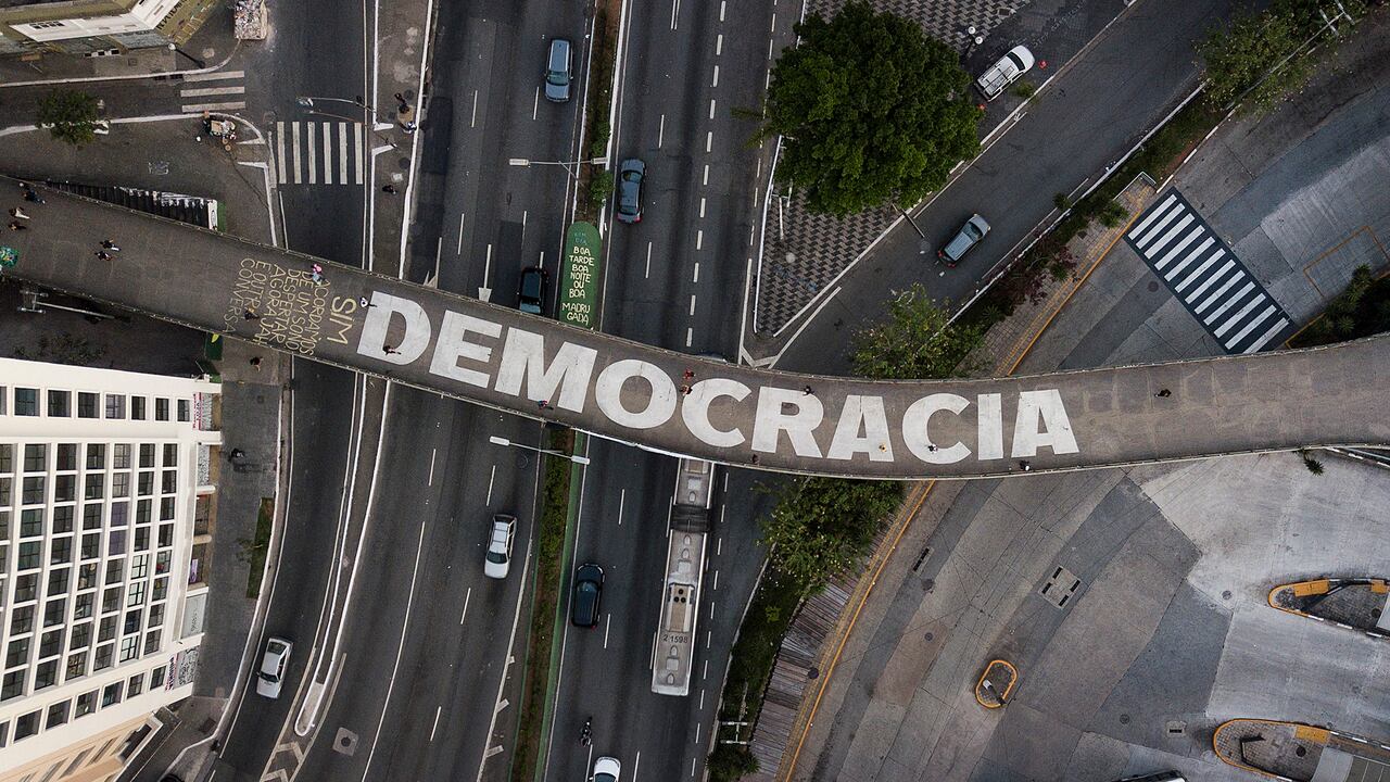 La gente camina por un puente peatonal que tiene un texto escrito que dice "Democracia" en portugués en Sao Paulo, Brasil, el miércoles 26 de octubre de 2022, días antes de la segunda vuelta que le dio la victoria a Lula da Silva.