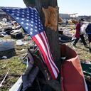 Una bandera cuelga de un árbol mientras dos mujeres llevan artículos recuperados de los restos del tornado el domingo 12 de diciembre de 2021 en Mayfield, Kentucky.