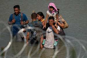 Migrants stand in the Rio Grande behind concertina wire as they try to enter the U.S. from Mexico near the site where workers are assembling large buoys to be used as a border barrier in Eagle Pass, Texas, Tuesday, July 11, 2023. The floating barrier is being deployed in an effort to block migrants from entering Texas from Mexico. (AP Photo/Eric Gay)