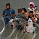 Migrants stand in the Rio Grande behind concertina wire as they try to enter the U.S. from Mexico near the site where workers are assembling large buoys to be used as a border barrier in Eagle Pass, Texas, Tuesday, July 11, 2023. The floating barrier is being deployed in an effort to block migrants from entering Texas from Mexico. (AP Photo/Eric Gay)