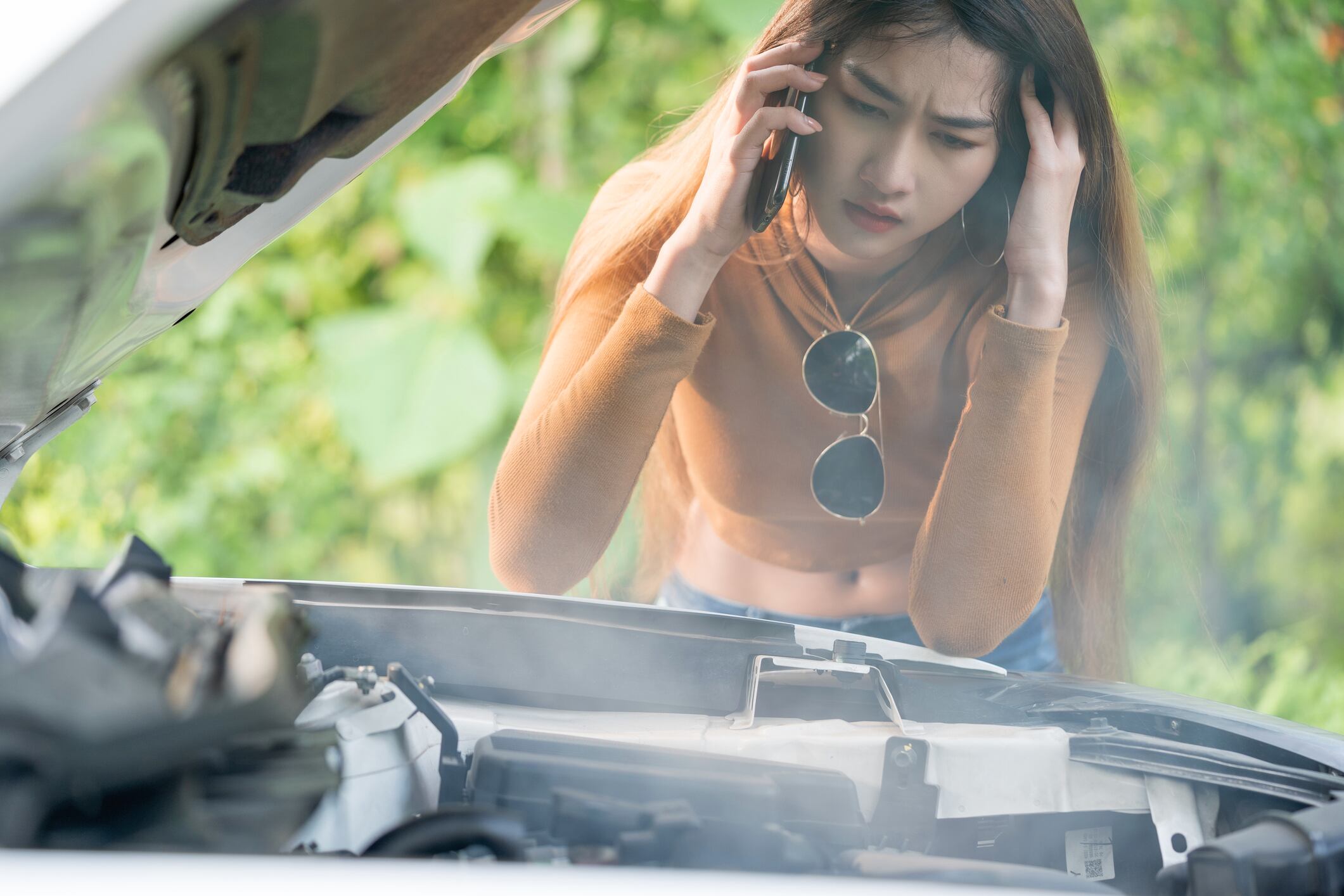 Woman having problem with her car engine overheat, it stopped on the street. She is calling for help wuth her mobile phone.