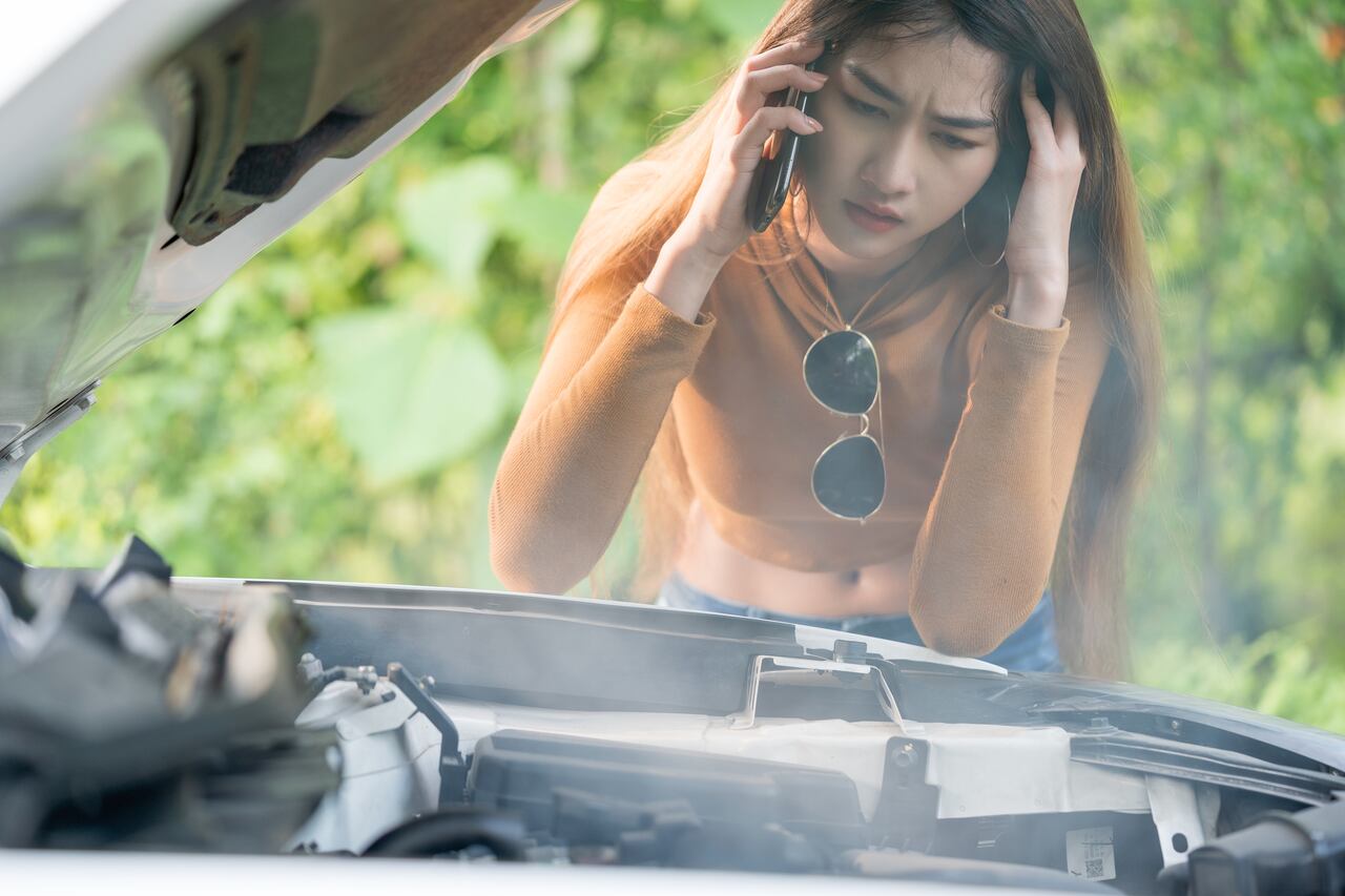 Woman having problem with her car engine overheat, it stopped on the street. She is calling for help wuth her mobile phone.