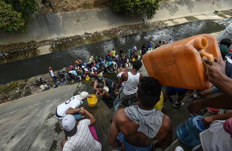 Las personas recolectan agua de una tubería rota, que fluye hacia un canal de aguas residuales en el río Guaire en Caracas. FOTO: JUAN BARRETO/AFP