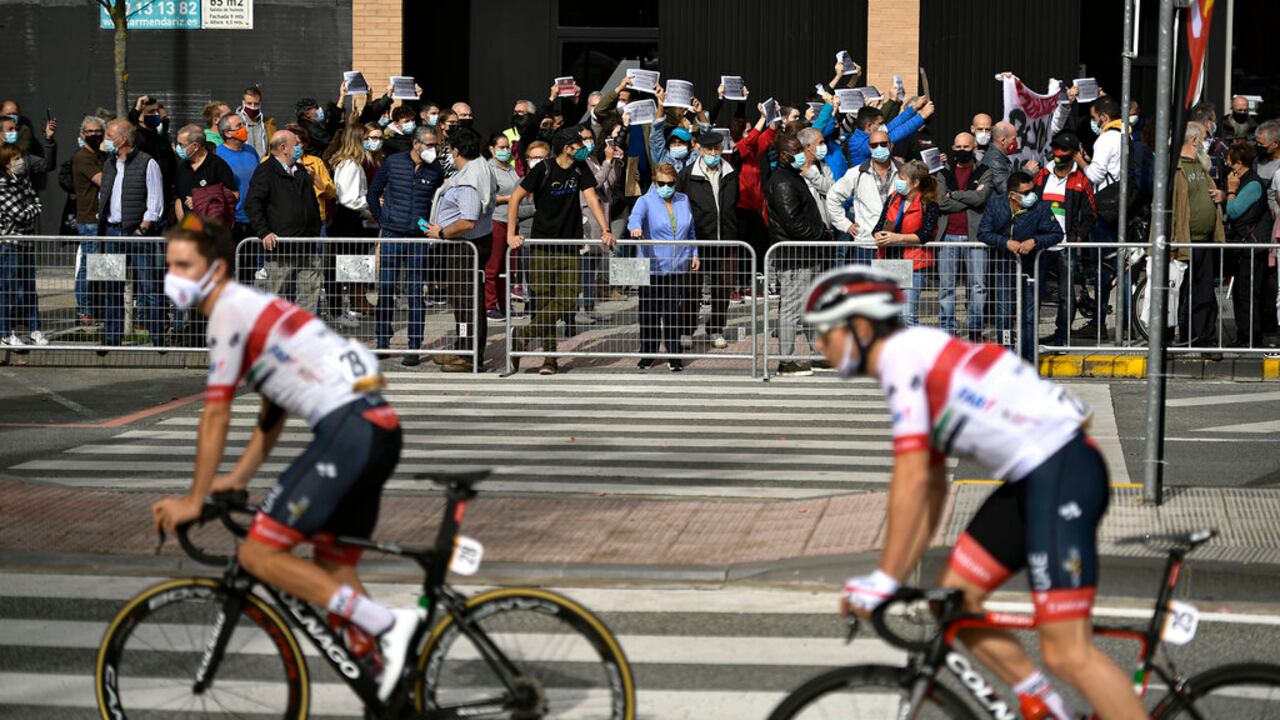 La Vuelta's cyclists pass people protesting against the new measures against the coronavirus in Navarra province, where all bar and restaurants will be closing during 15 days from midnight of today, before the second stage of La Vuelta between Pamplona and Lekunberri, in Pamplona, northern Spain, Wednesday, Oct. 21, 2020. (AP Photo/Alvaro Barrientos)