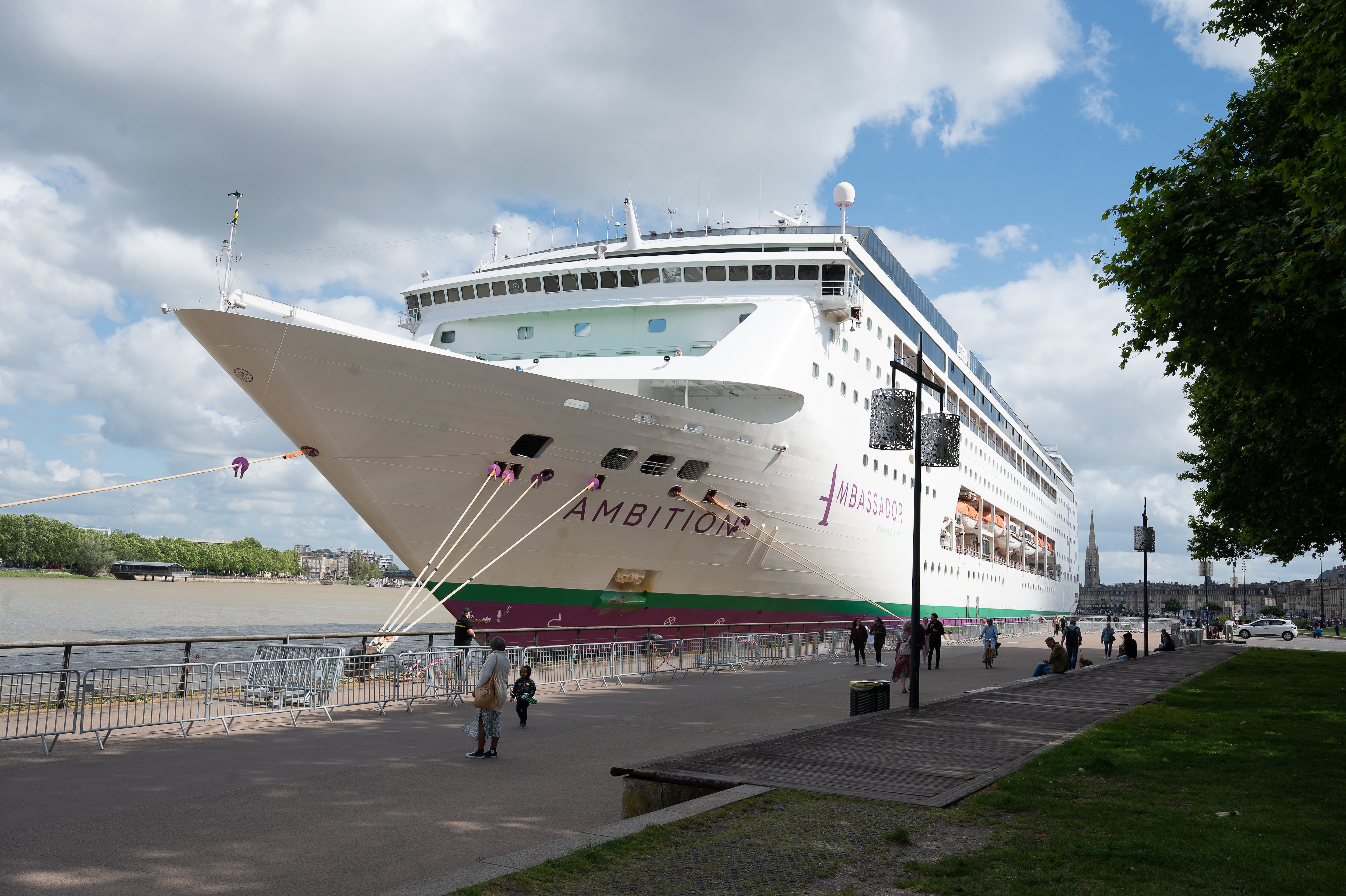 La gente pasa junto al crucero británico Ambition, mientras las autoridades francesas ordenaron a 1.700 pasajeros y tripulantes permanecer a bordo debido a un brote de enfermedad gastrointestinal, en Burdeos, suroeste de Francia, el miércoles 13 de mayo de 2026. (Foto AP/Caroline Blumberg)