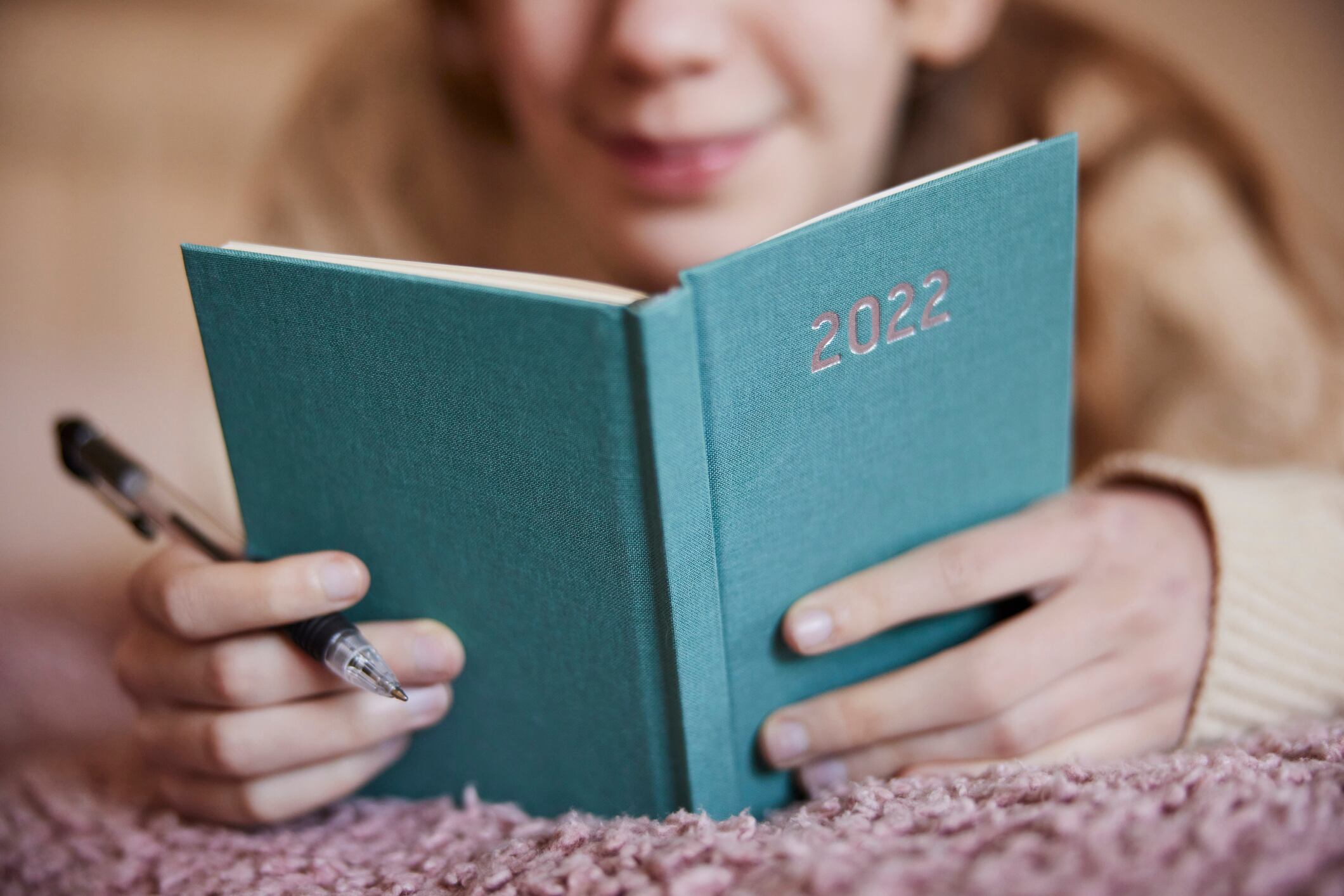Primer plano de una adolescente acostada en la cama escribiendo en un diario de 2022
