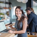 Mujer de negocios feliz trabajando en un café en una computadora portátil y mirando a la cámara sonriendo. La imagen en pantalla es de diseño propio.