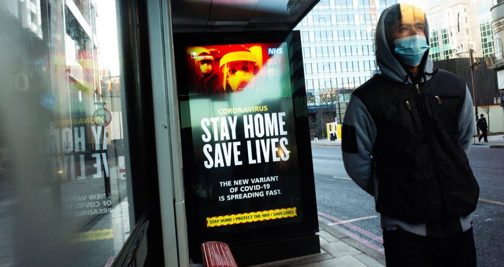 Un joven espera junto a los mensajes del gobierno que dicen a las personas que se queden en casa, exhibidos en una parada de autobús en Londres, Inglaterra.