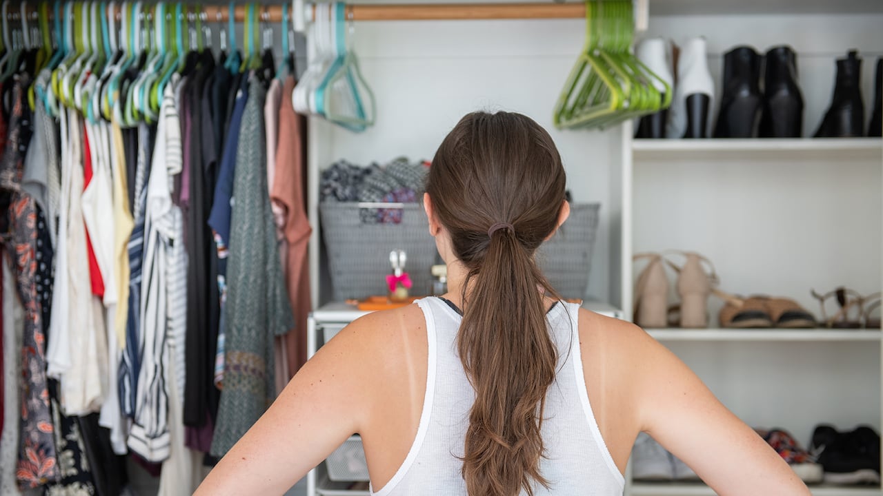 Esta es una joven adulta con las manos en las caderas tratando de decidir qué ponerse de su armario bien organizado.