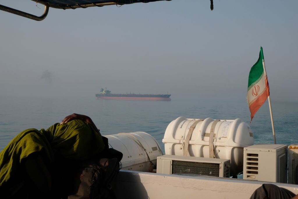 Un turista extranjero descansa en un barco de pasajeros con la bandera iraní en las aguas del Estrecho de Ormuz el 2 de mayo de 2017 cerca de la isla de Hormuz, Irán. Al fondo se ve un petrolero en movimiento. (Foto de Kaveh Kazemi/Getty Images)
