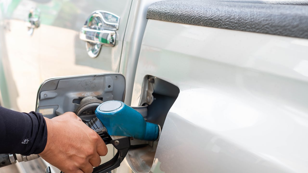 The hand is holding the nozzle to refuel the car in the gas station.