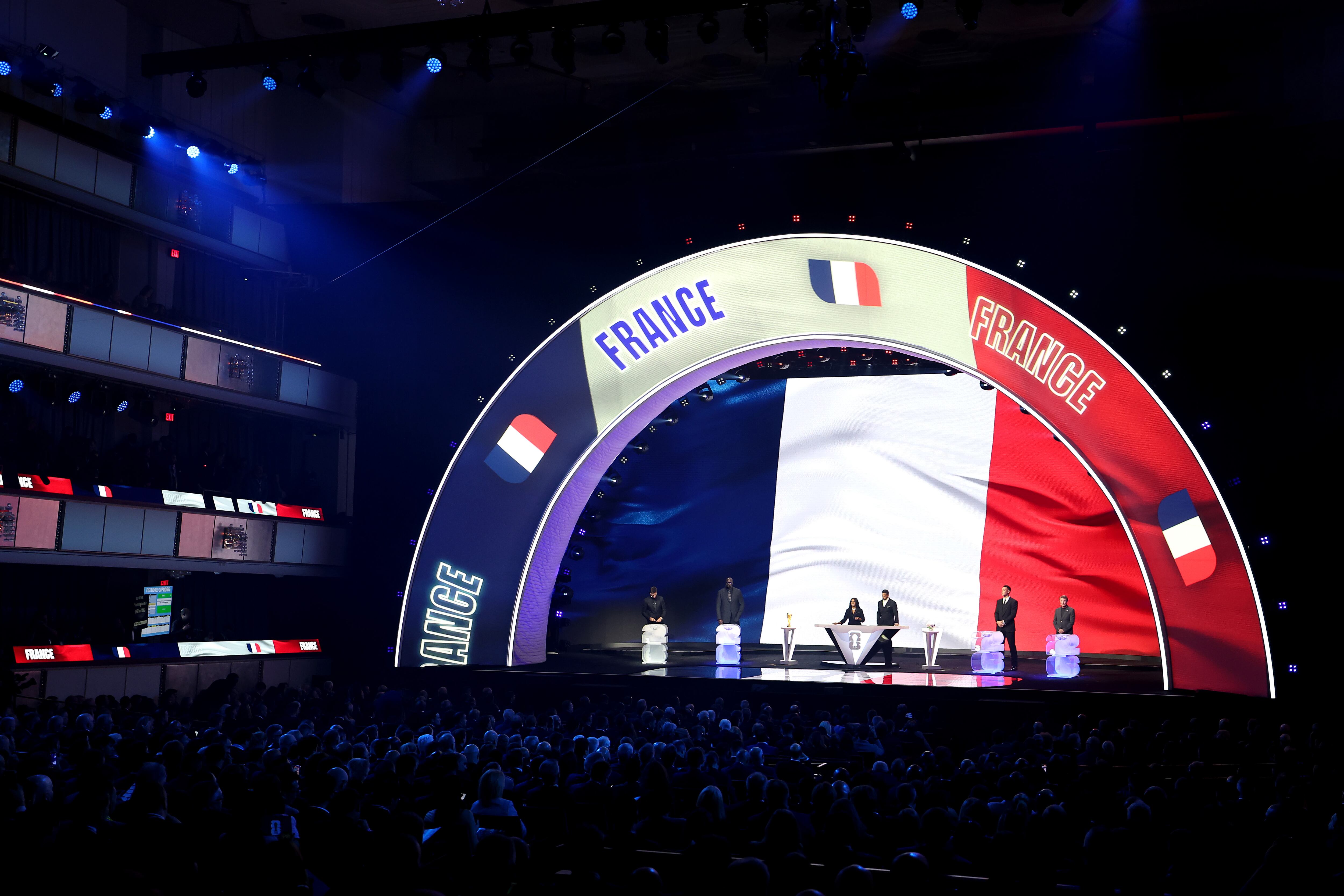 El asistente de sorteo Tom Brady, el asistente de sorteo Shaquille O'Neal, la codirectora Samantha Johnson, la leyenda de la FIFA Rio Ferdinand, el asistente de sorteo Aaron Judge y el asistente de sorteo Wayne Gretzky están en el escenario mientras Francia se ilumina en la pantalla durante el sorteo oficial de la Copa Mundial de la FIFA 2026 en el Centro John F. Kennedy.