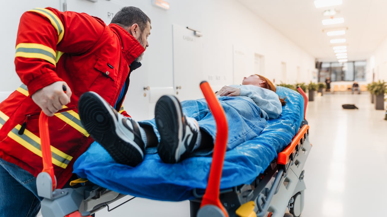 Paramédico masculino uniformado empuja a un paciente en camilla a través del pasillo del hospital hacia la sala de emergencias.