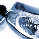 Close up of the head lights of a new car. The color of the car is silver metallic, blue. The background is white. Front view, left wing. photographed with a 50mm prime lens and full frame camera.modern car-light, isolated on white, toned image