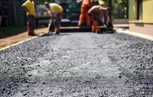 Team of Workers making and constructing asphalt road construction with finisher. The top layer of asphalt road on a private residence house driveway