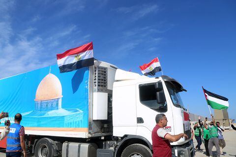 La gente en el lado egipcio del cruce fronterizo de Rafah aplaude mientras un convoy de camiones que transportan ayuda humanitaria cruza hacia la Franja de Gaza el 21 de octubre de 2023. El primero de 20 camiones que transportaban ayuda humanitaria entró en la Franja de Gaza asediada y devastada por la guerra el 21 de octubre.