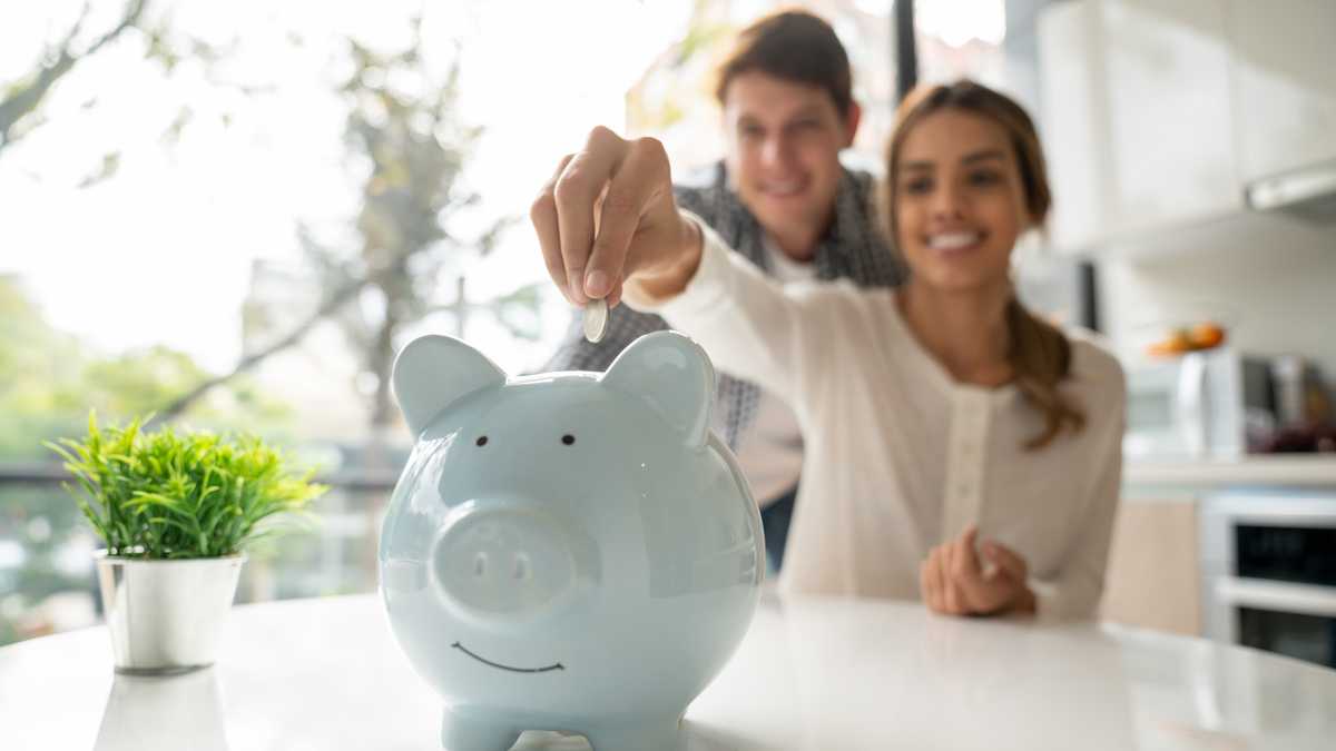 Focus on foreground of latin american young couple saving coins into piggy bank - Lifestyles
