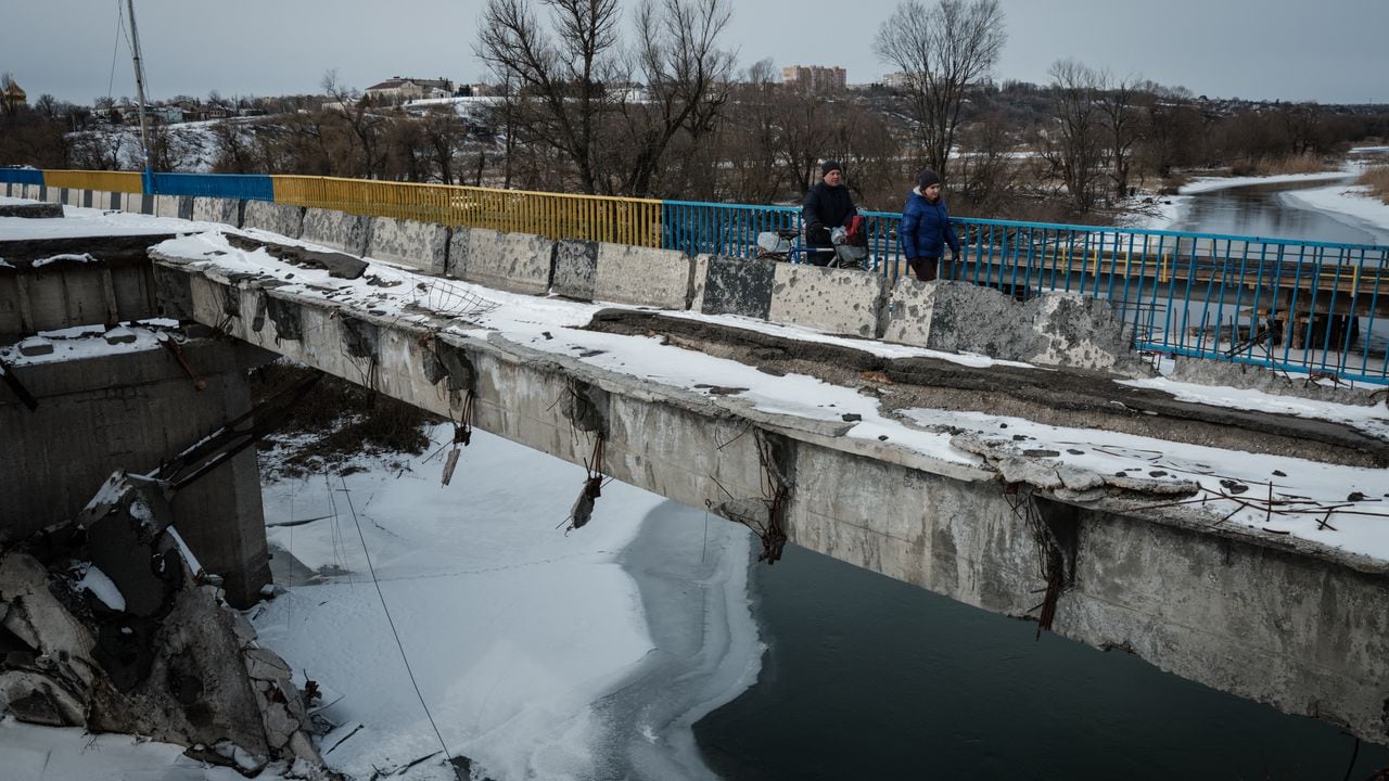 Elena (derecha) y Petr cruzan un puente destruido después de recolectar agua potable de un punto de distribución en Kupiansk el 13 de febrero de 2023, en medio de la invasión rusa de Ucrania. (Foto de YASUYOSHI CHIBA / AFP)