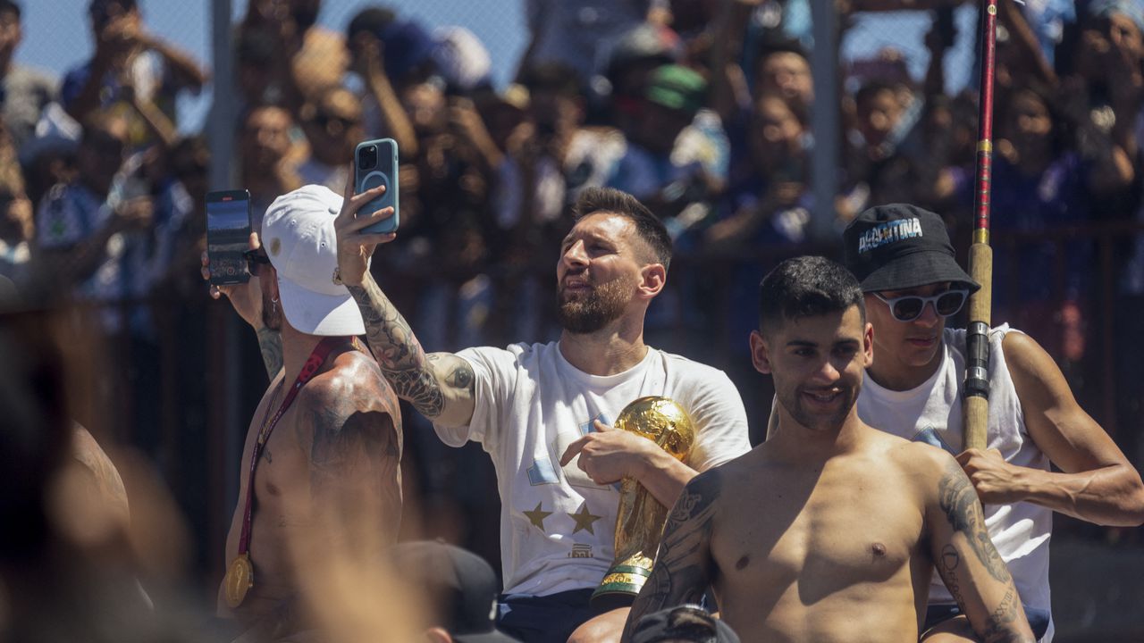 Argentine football star Lionel Messi (C) takes pictures with his phone while celebrating on board a bus with a sign reading "World Champions" with supporters after winning the Qatar 2022 World Cup tournament as they tour through Buenos Aires' downtown on December 20, 2022. - Millions of ecstatic fans are expected to cheer on their heroes as Argentina's World Cup winners led by captain Lionel Messi began their open-top bus parade of the capital Buenos Aires on Tuesday following their sensational victory over France. (Photo by TOMAS CUESTA / AFP)