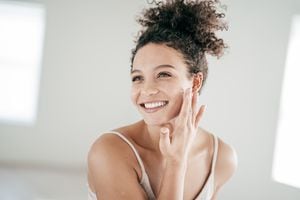 Smiling young women applying moisturiser to her face
